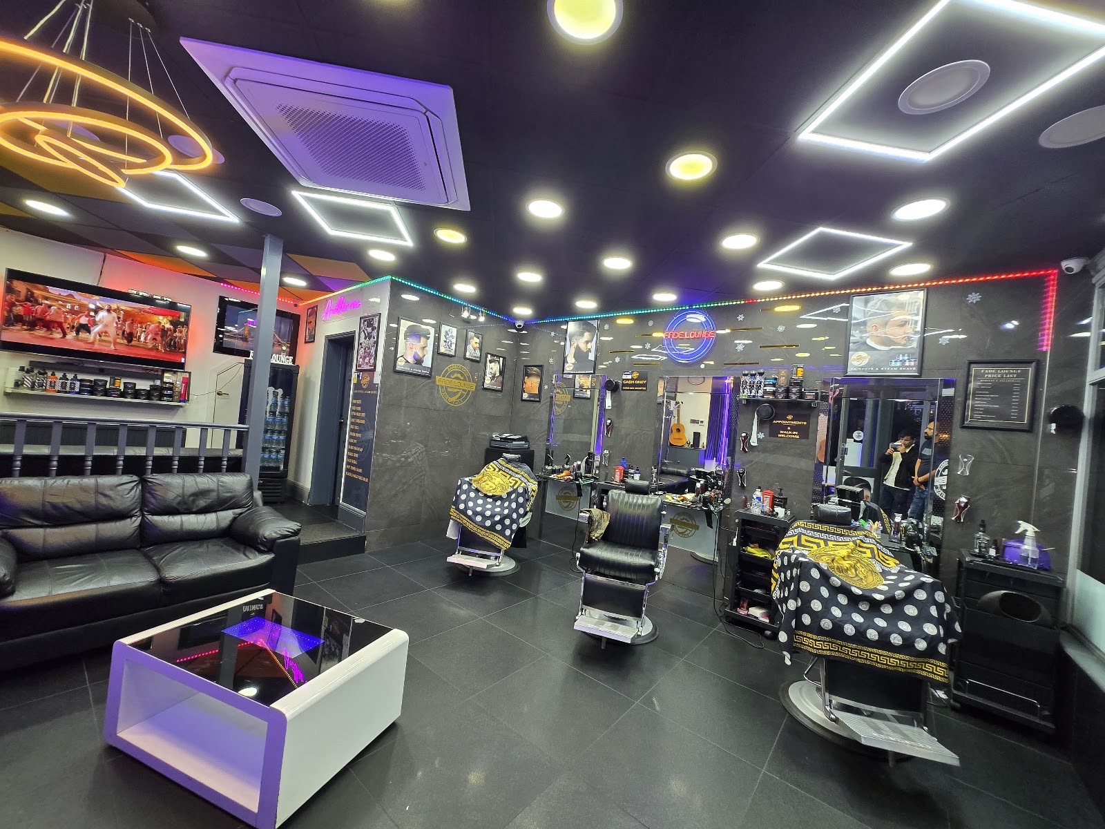 Wide interior of the barbershop, chairs and mirrors lit by purple and white neon